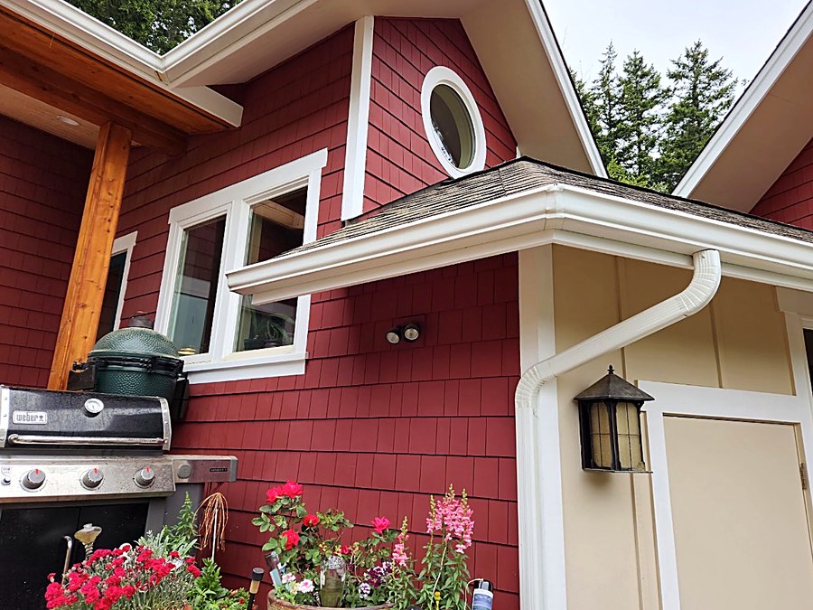 Close-up of freshly painted deep red shingle siding meeting a cream board-and-batten wall, with white trim, a round window and a lantern porch light.